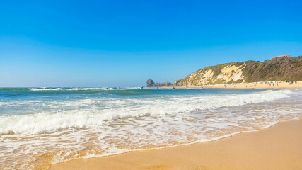 Beautiful coastal scene showcasing a sandy beach, gentle waves, and a clear blue sky. Ideal for travel, vacation, or relaxation concepts. Evokes a sense of peace and tranquility.