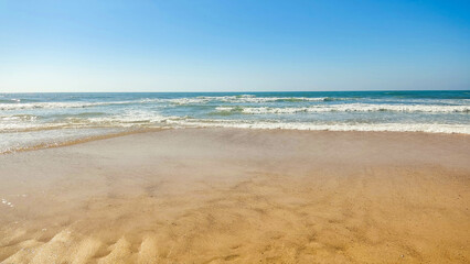 Serene ocean scene. Golden sand meets gentle waves under a clear blue sky. Evokes peace, relaxation,  summer vibes. Ideal for travel, wellness, or lifestyle content.