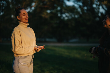 Warm interaction between two women at a grassy outdoor setting during golden hour, showcasing their friendly conversation and relaxed atmosphere, with shadows enhancing the ambient mood of the moment.