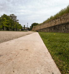 An eyelevel shot of a path with stone edges, juxtaposing gravel and grass under a cloudy sky. Captures nature meeting urban design. Suitable for environmental or travel themes.