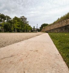 Perspective shot of a pathway through a park, contrasting gravel, pavement, and grass. A historic wall frames the scene, hinting at resilience and exploration.