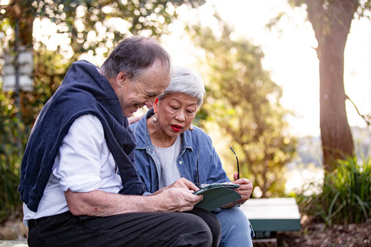 Senior couple sitting at park bench looking at computer tablet