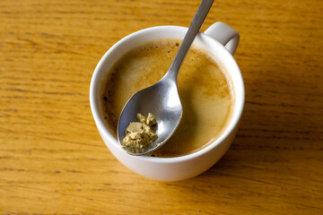 Cup of coffee on a wooden table, ground ginger on a spoon, coffee with the addition of ginger stimulating digestion.