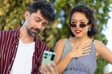 Two friends sharing a moment looking at a smartphone outdoors on a sunny day, showcasing connection and technology in a social setting.
