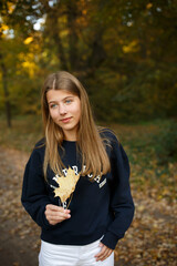 Young woman in dark sweatshirt and white pants standing on a quiet autumn street. Golden foliage...
