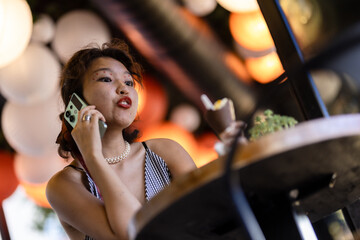 Young woman talking on smartphone in a cafe, enjoying a dessert, surrounded by warm ambient lighting on a relaxed afternoon