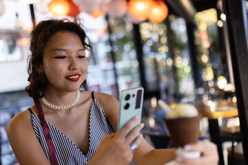 Young woman enjoying ice cream at a cafe while using her smartphone for taking a picture. Capturing casual moments of summer leisure with stylish makeup and fashion.