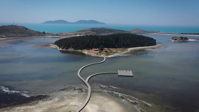 Forward drone shot of Zverneci Island in Narta Lagoon, Albania, crossing the wooden bridge and ending with a downward tilt revealing the iconic monastery and surrounding pine forest.