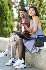 Casual outdoor meeting of two diverse friends smiling and sharing ideas with a laptop in a park setting