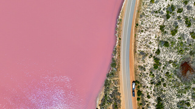 Aerial of caravan on road next to pink lake