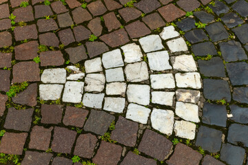 Intricate patterns of cobblestone with green grass peeking through in an old town square at sunset