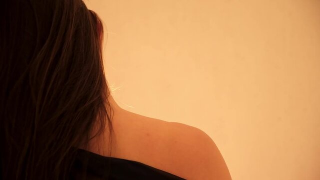 A sexy undressing woman takes off her silk negligee exposing shoulder. Seductive erotic movements of the female body rear view close-up. Sexual foreplay of arousal. A brunette with long straight hair.