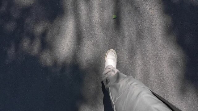 A man in trousers walks along the sidewalk, an overhead view of men's legs