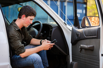 concerned teenaged Australian young man sitting in his ute holding mobile phone device