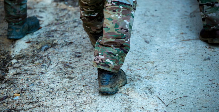 Soldier wearing camouflage pants and boots walking on a dirt road