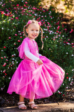 Happy little girl in pink fancy dress in garden swirling skirts