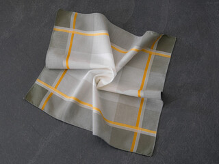 Elegant folded handkerchief with striped design, displayed on a dark stone surface. Suitable for concepts related to men’s fashion accessories, style, or fabric textures.
