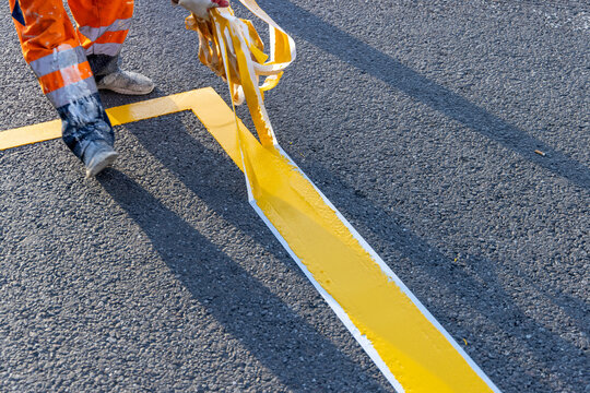 Road worker applying yellow road markings to asphalt using stencil tape. Close-up of a road worker applying yellow paint to asphalt with stencil tape
