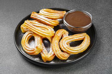 Traditional spanish dessert churros, fried dough pastry dusted with powdered sugar and chocolate sause on black background. Street food, sweet snack, homemade dessert.
