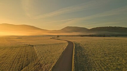 Fototapeta premium An aerial view of a winding road through a vast, foggy field with distant mountains, creating a serene and peaceful atmosphere for outdoor enthusiasts and cyclists.
