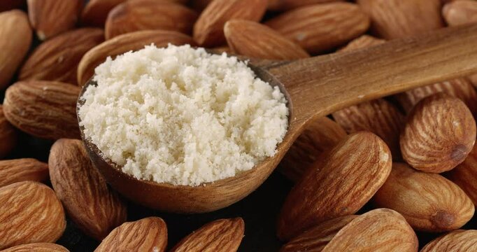 Wooden spoon with almond flour on a background of almond nuts. Close-up footage on the rotating table.