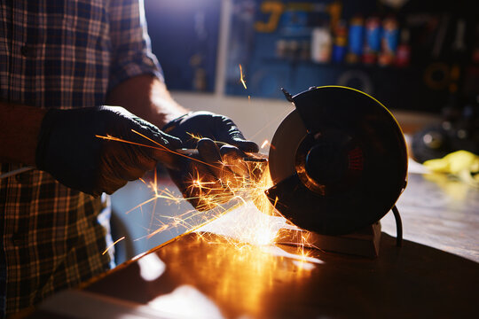 Mechanic sharpening metal part with bench grinder creating sparks in workshop