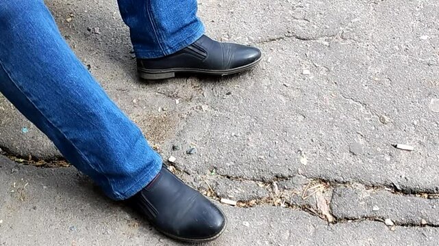 A man sitting down, nervously beating out a rhythm on the pavement with his foot, showing impatience and anticipation