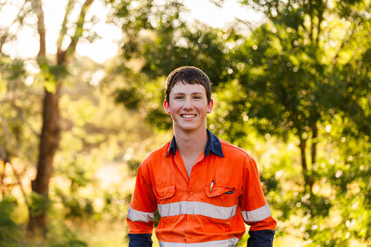 Portrait of happy young tradesman apprentice in high vis workwear against leafy green bokeh backdrop