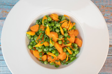 Fresh garden peas and carrots are cooked with salted butter, then garnished with chives and bright marigold flowers for an appealing and colorful side dish.