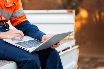 Young trainee tradie apprentice working on laptop in back of ute in high-vis workwear