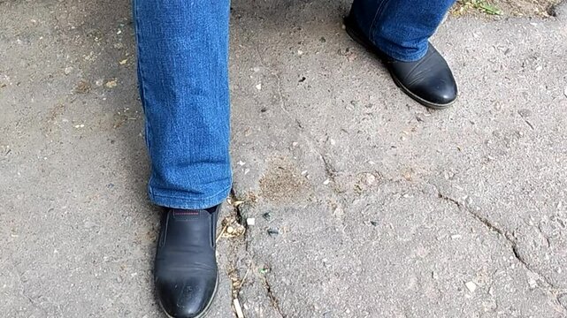 A man sitting down, nervously beating out a rhythm on the pavement with his foot, showing impatience and anticipation