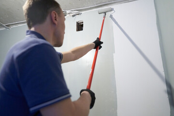 A man paints concrete walls with a paint roller. Gray paint creates a cozy atmosphere in the room. High quality photo
