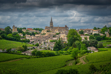Naklejka premium Springtime brings vibrant greenery to the Bordeaux vineyards surrounding the charming village of Saint-Emilion, showcasing picturesque hills and historical architecture.