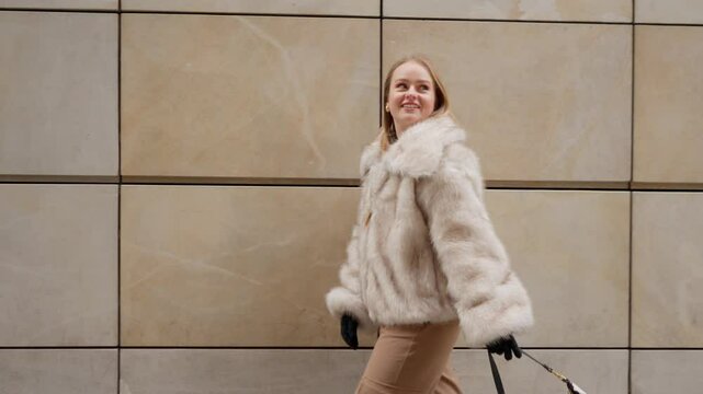 A beautiful woman demonstrates her elegant winter fashion, walking on a city street. Her fur coat is perfect for the mild, snowless European winter, a concept of seasonal style.
