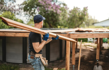 Handyman worker making patio outside close to a pool holding wood