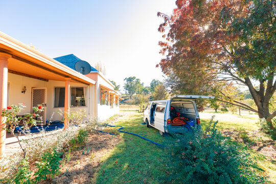 Small white van with commercial carpet steam cleaning equipment parked outside home with blue hoses