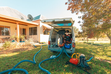 Professional man inside van with commercial carpet steam cleaning equipment parked outside home