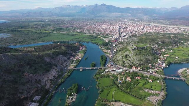 Rightward-moving drone shot over the Buna River in Shkoder, Albania, gradually revealing the vast expanse of Lake Shkodra, with the city, Rozafa Castle, and lush landscapes in view.