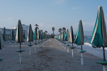 Closed umbrellas on sandy beach in Sardinia, Poetto shore with summer mood and calm coastal atmosphere