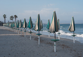 Closed umbrellas on sandy beach in Sardinia, Poetto shore with summer mood and calm coastal atmosphere