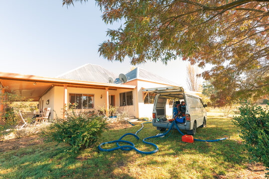 Small white van with commercial carpet steam cleaning equipment parked outside home with hoses