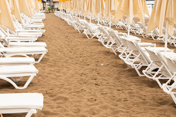 Beach scene with empty closed umbrellas and sun loungers on on sea shore