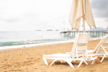Beach scene with empty closed umbrellas and sun loungers on on sea shore
