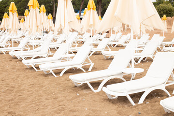 Beach scene with empty closed umbrellas and sun loungers on on sea shore