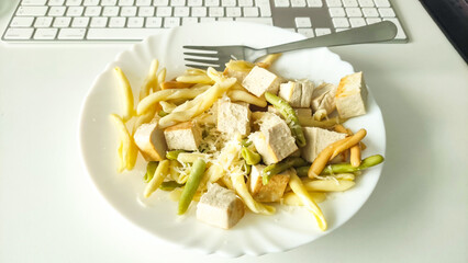 Office worker eating vegan pasta with tofu and green beans at lunch break