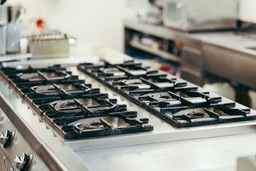 Close-up of a clean industrial gas stove in a professional kitchen. Stainless steel surfaces and control knobs emphasize cleanliness and commercial use.