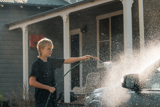 Teenage boy hosing down vehicle in preparation for cleaning car
