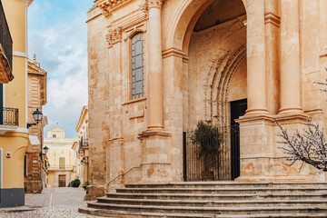 An elegant side entrance of the Ciutadella de Menorca Cathedral, featuring grand columns, an arched doorway, and intricate stone detailing. The blend of styles in Menorca religious landmark