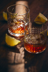 Glasses of whiskey with ice and lemon slices on a wooden table in the rays of light. Shallow depth of field, close up.