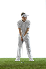 Young male golfer dressed in all-white attire standing on green grass, focusing before hitting ball...